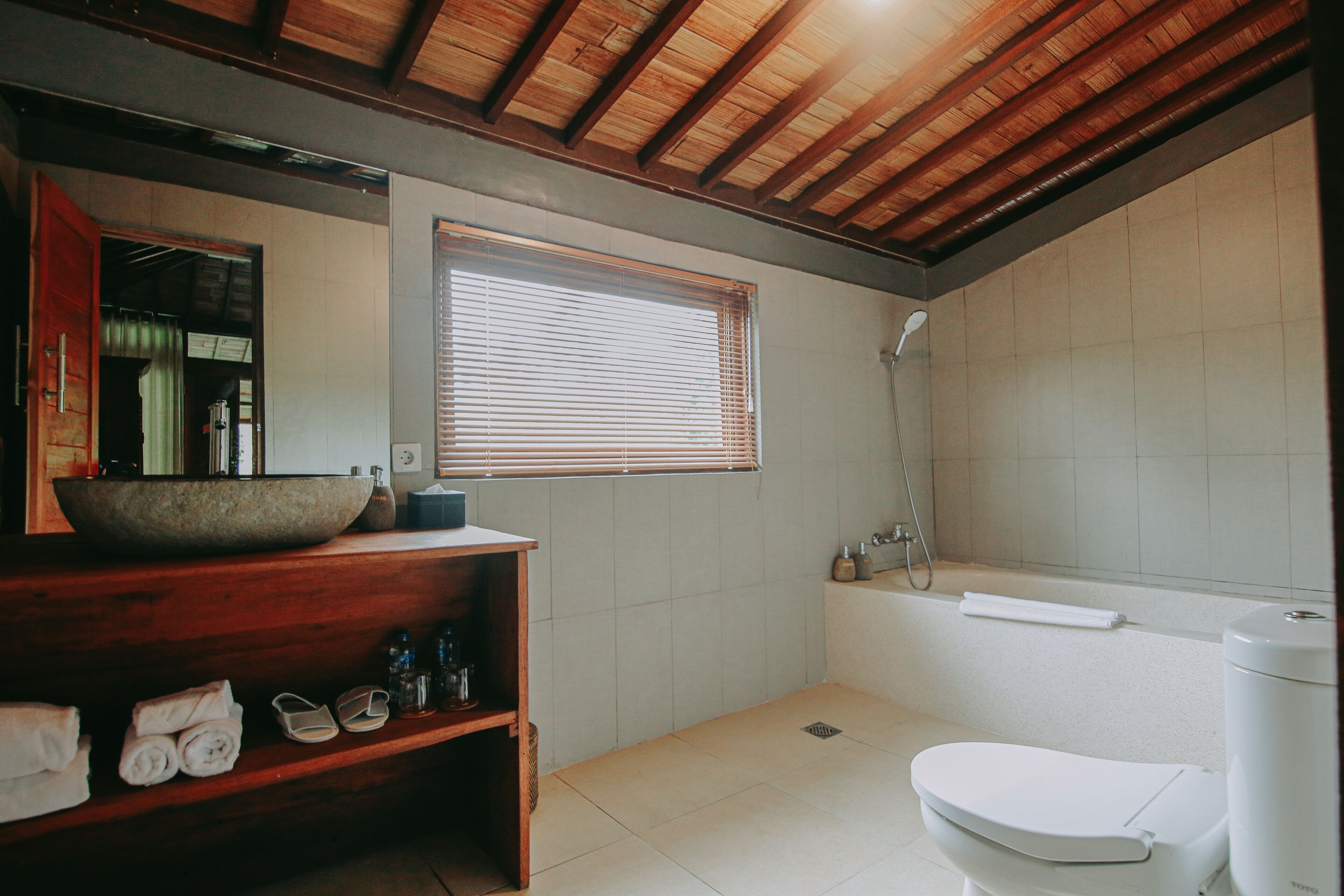 Un baño con tocador de madera, un lavabo grande tipo cuenco, inodoro y bañera.