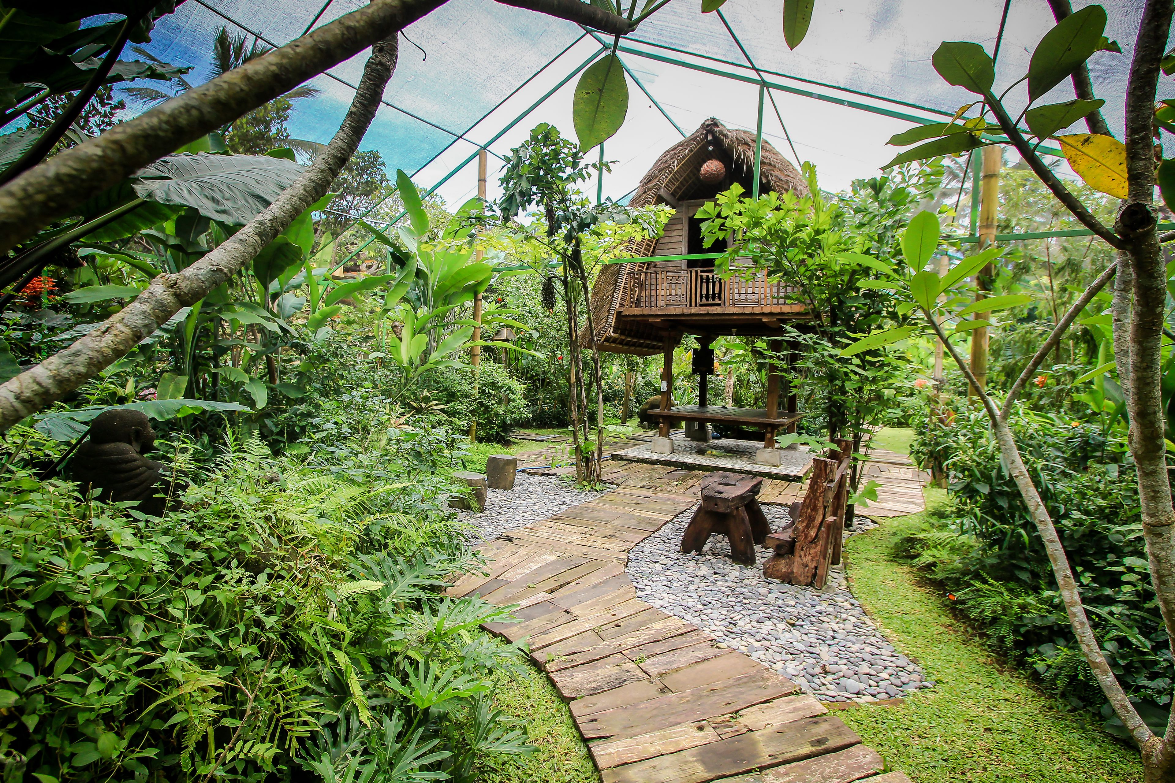 Un jardín tropical con una terraza de madera, una estructura con techo de paja y follaje denso.