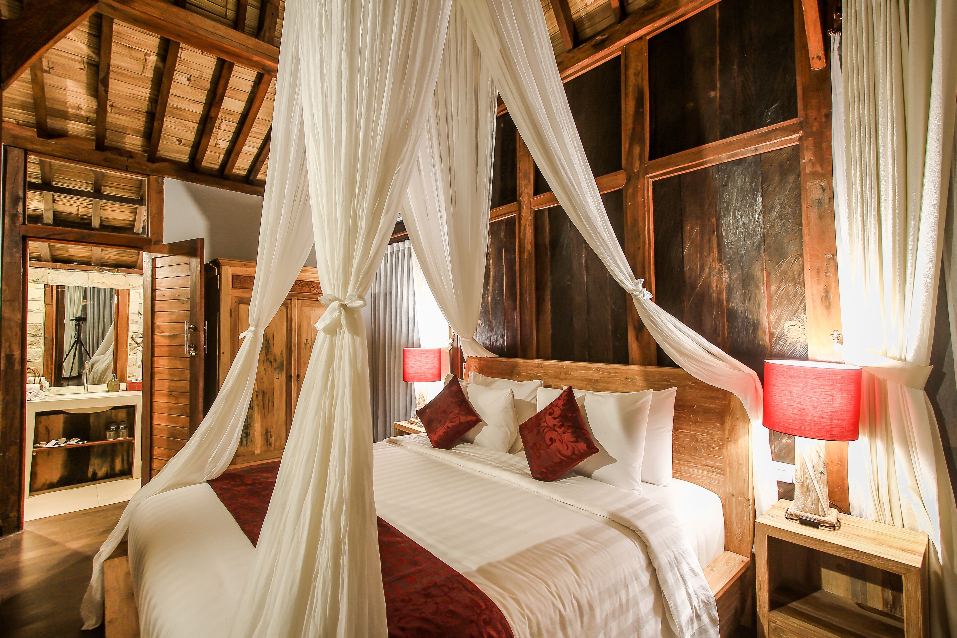 Ein Schlafzimmer mit Himmelbett, Holz-Kopfteil, Nachttischen mit Lampen und einem Spiegel.