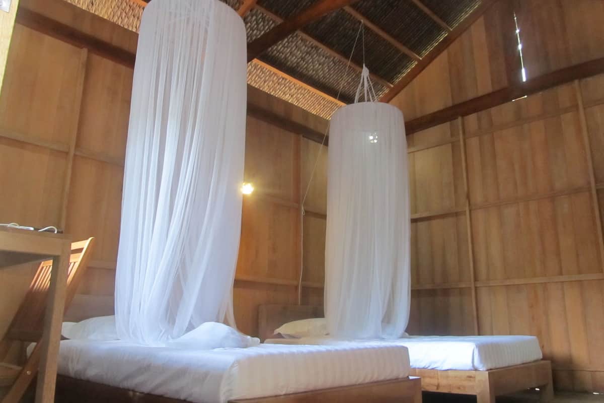Dos camas de madera con ropa blanca y cortinas blancas colgadas.