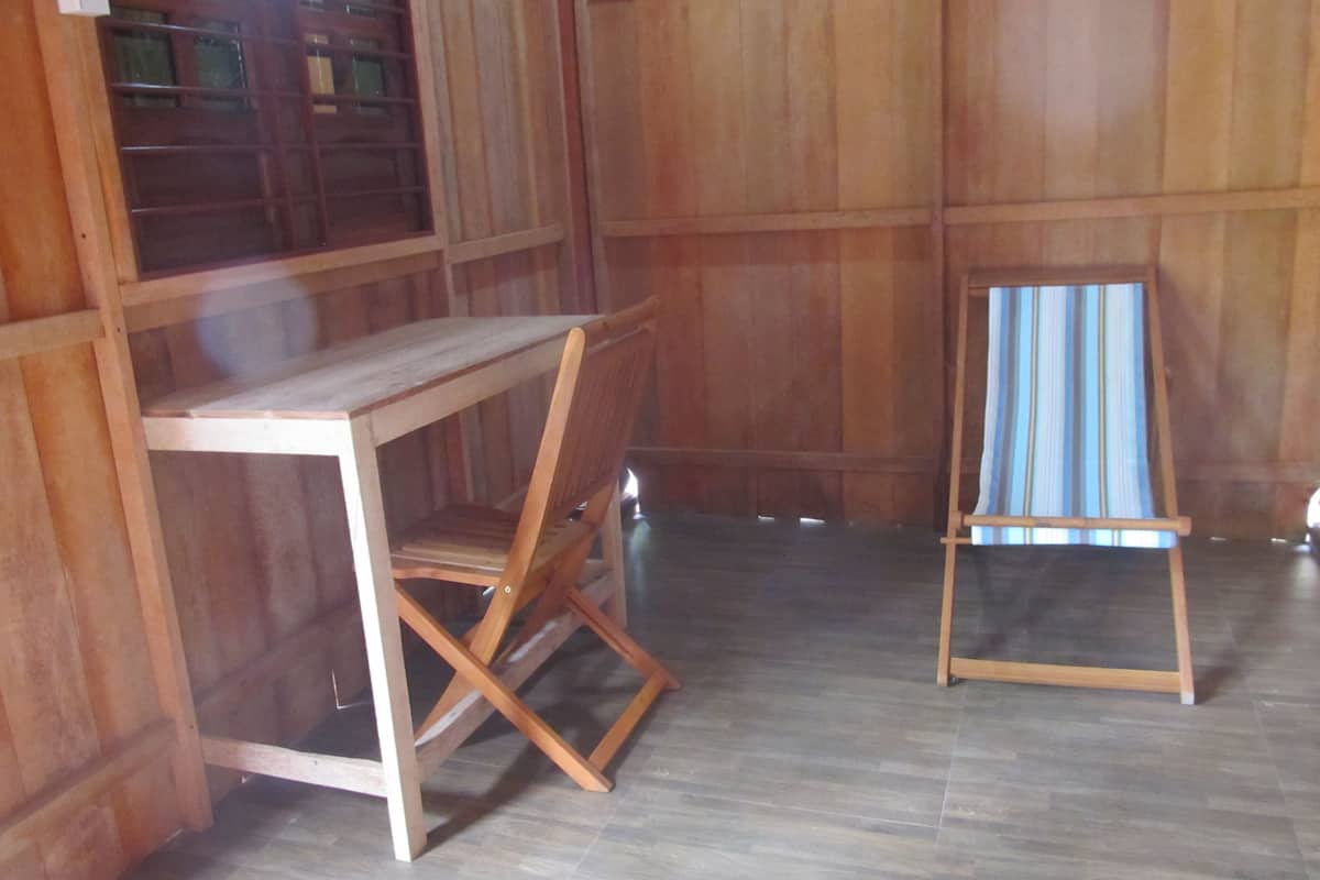 Una habitación con un escritorio y una silla de madera, un caballete pequeño y una ventana con persianas.
