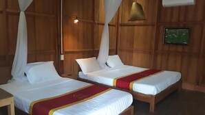 Une pièce avec deux lits en bois, chacun recouvert d’une literie blanche et d’une couvre-lit rouge et jaune. Les murs sont recouverts de lambris en bois et un climatiseur est fixé au mur.
