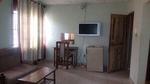 Un salon avec un canapé, une table en bois, un téléviseur fixé au mur et une porte.