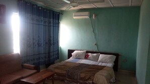 Une pièce comprenant un lit, un banc en bois, un ventilateur de plafond et un appareil de climatisation.