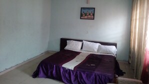 Une chambre à coucher avec un lit, un ventilateur de plafond, un tableau encadré au mur et une fenêtre avec des rideaux.