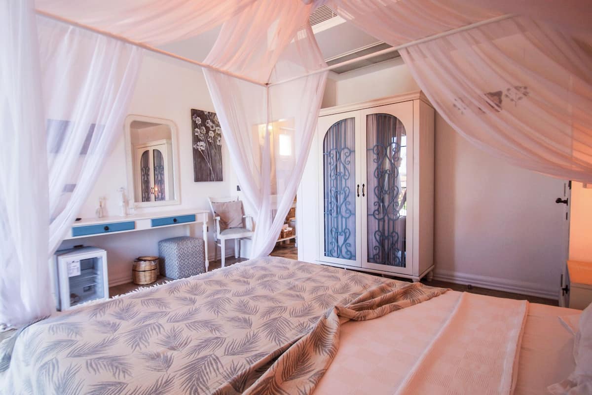 A bedroom with a canopy bed, a wardrobe, a desk, and a chair.