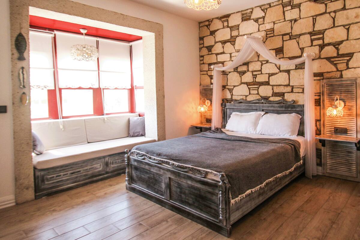 A bedroom with a stone wall, a bed with a canopy, and a bench by the window.