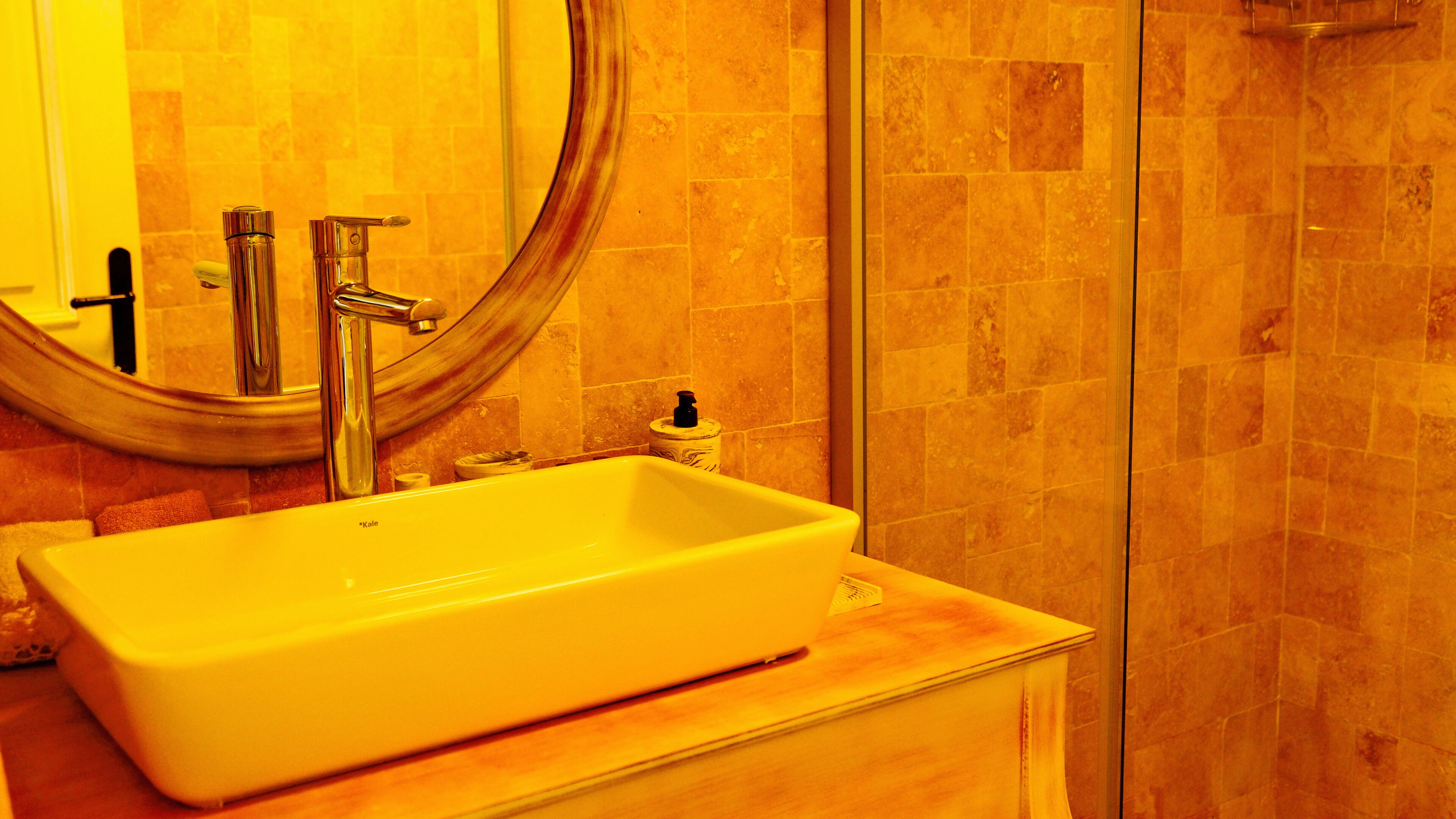 Ein Badezimmer mit einem rechteckigen Waschbecken, einem Spiegel und einer Duschkabine.