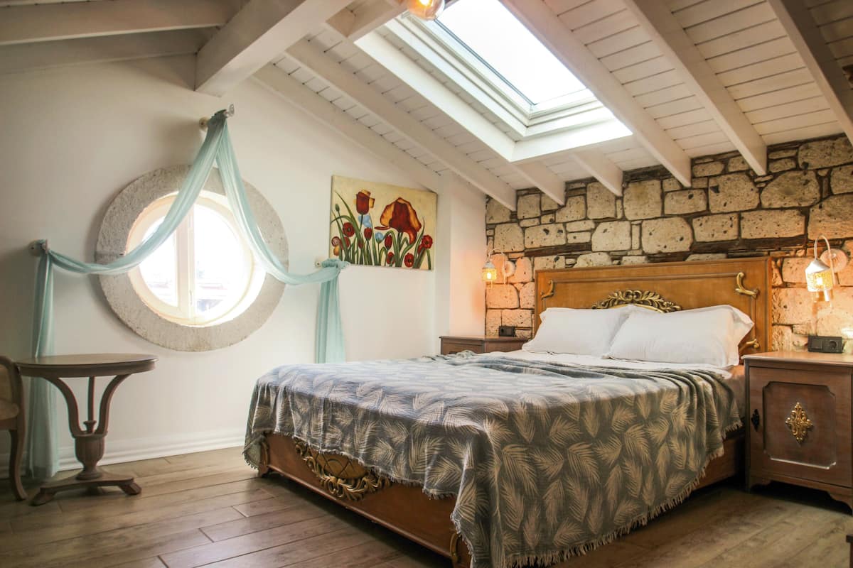 A bedroom with a wooden bed, a stone wall, a skylight, and a round window with curtains.