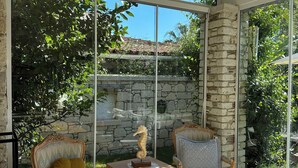 A sunlit room with large windows, a stone wall, and two ornate chairs with cushions.