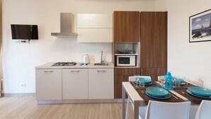 A modern kitchen with a gas stove, microwave, and a dining area with blue plates and glasses. - Modern Apartment "Gennaker" On Lakeside with Terrace and View (Malcesine)