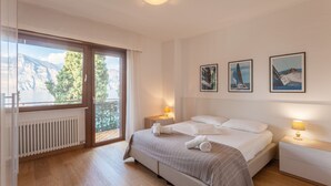 A bedroom with a bed, two bedside tables, a window with a view, and three framed pictures on the wall. - Modern Apartment "Gennaker" On Lakeside with Terrace and View (Malcesine)