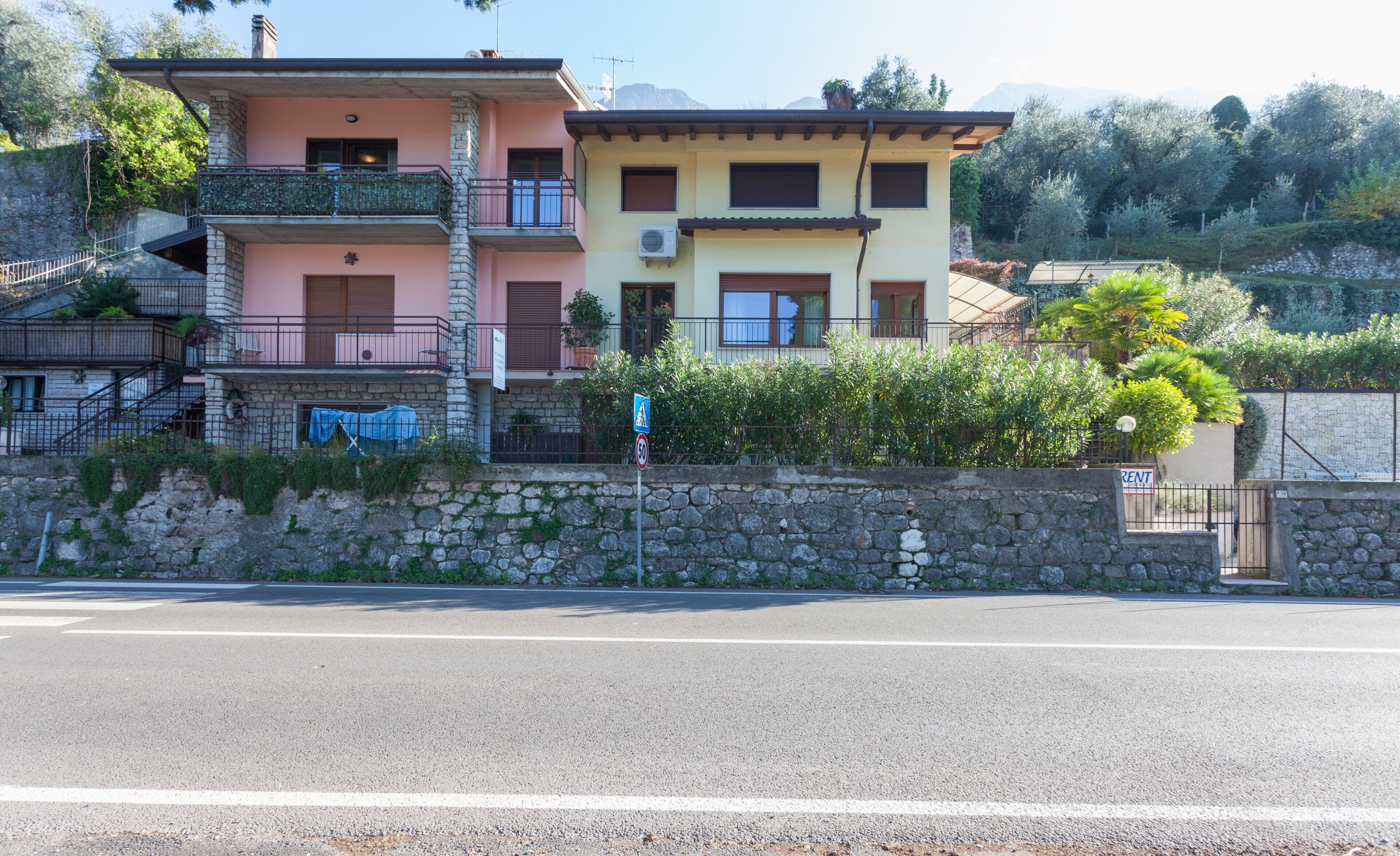 Un edificio residencial de varios pisos con balcones, un muro de piedra y una calle despejada al frente.