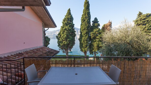 A patio with a table and chairs, overlooking a body of water and trees. - Modern Apartment "Gennaker" On Lakeside with Terrace and View (Malcesine)