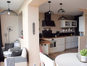 Une cuisine moderne avec des meubles blancs, des appareils électroménagers noirs et des luminaires suspendus.