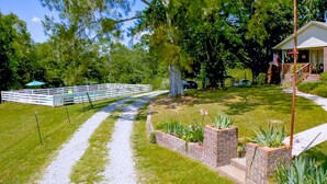 A pathway leading to a white fence, a brick planter with plants, and a building with a porch. - She's back! Under new management (Cullman)
