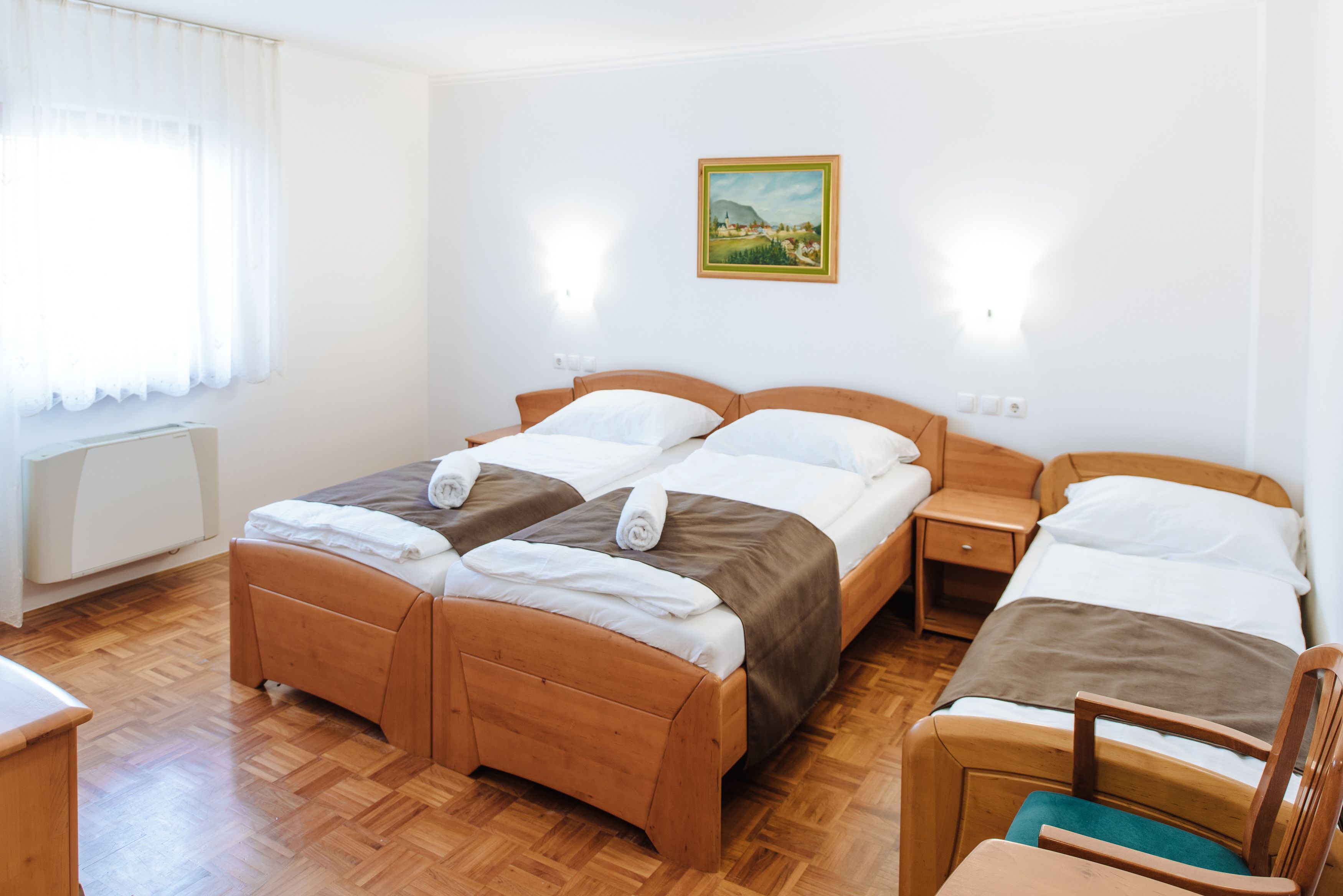 A room with two wooden beds, a wooden chair, a small table, and a radiator.