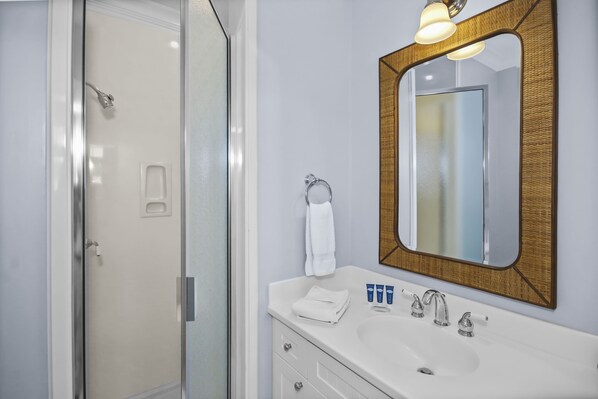 Un baño con mampara de vidrio, un lavabo blanco con dos grifos y un espejo con marco de madera.