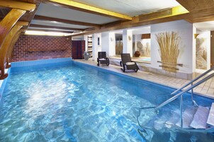 Una piscina con agua cristalina, vigas de madera y dos tumbonas.