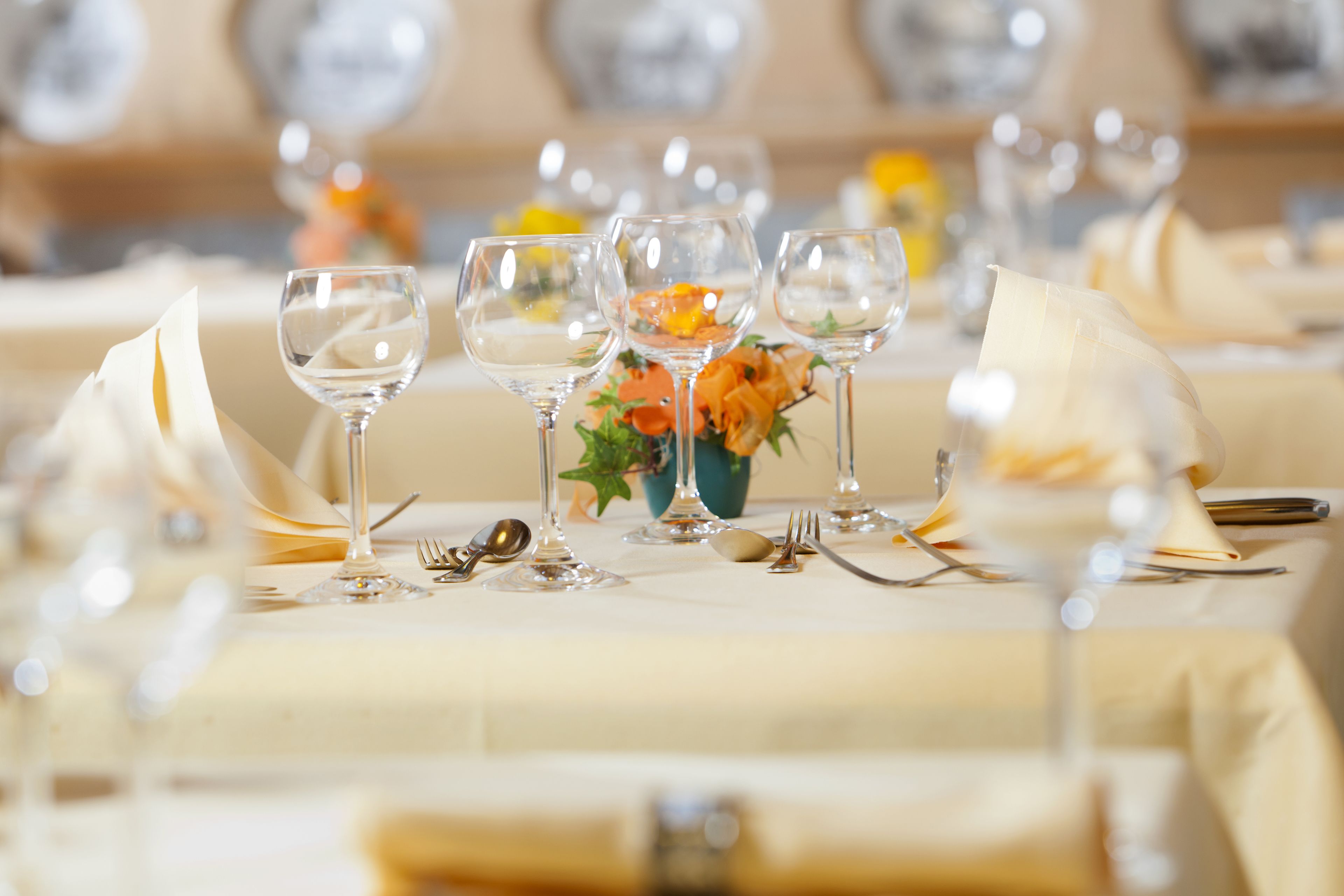 Una mesa de comedor dispuesta con copas de vino, cubiertos y un centro de mesa con flores.
