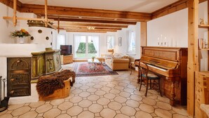 Ein geräumiges Wohnzimmer mit Holzbalkendecke, einem Klavier, einer Couch und einem Kamin.