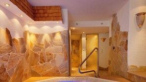 Ein Whirlpool mit Steinwand, Holzboden und Glastür zum Duschbereich.