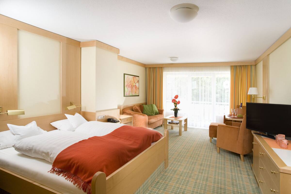 Una habitación de hotel con cama, sofá, escritorio con televisor y ventana con cortinas.