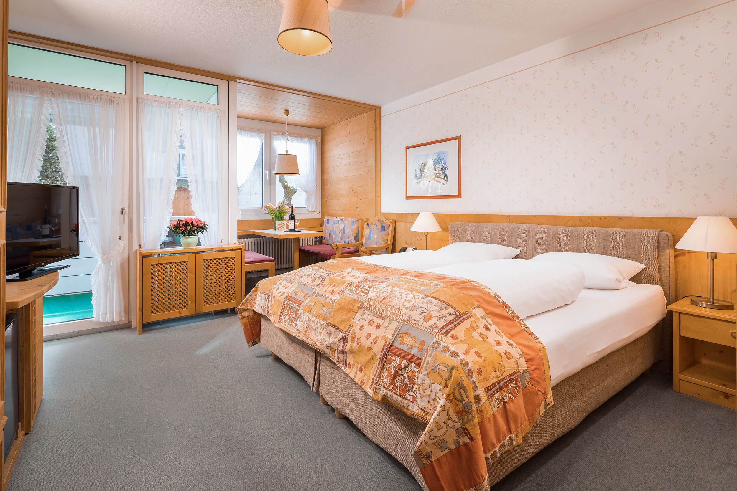 A hotel room with a bed, a TV, a desk, and a window with curtains.
