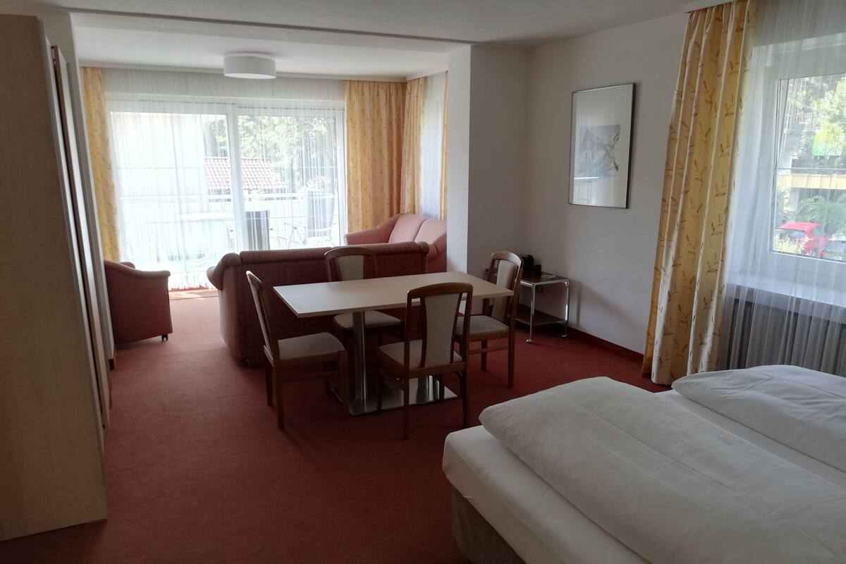 Una habitación de hotel con una cama, una mesa de comedor con sillas, un sofá y una mesita con una silla.