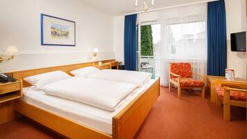 A hotel room with a wooden bed, two bedside tables, a chair, a desk, a television, and a window with curtains.