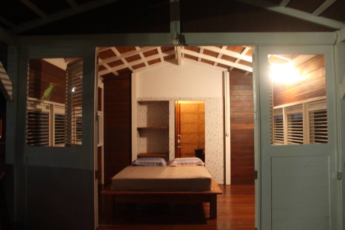 Une pièce avec un lit, une porte en bois et une fenêtre avec des volets.