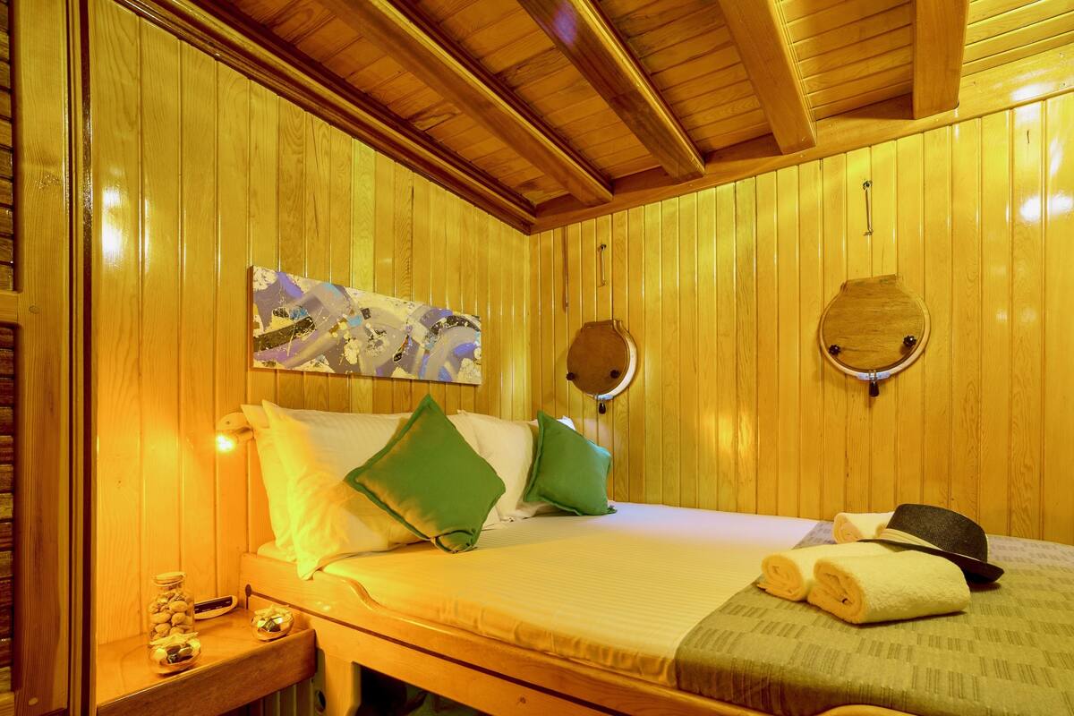 Ein Zimmer aus Holz mit einem Bett, Kissen, einem Gemälde, einem Spiegel und Handtüchern.