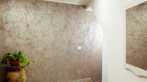 Um quarto com parede texturizada, um vaso com planta e piso de madeira.