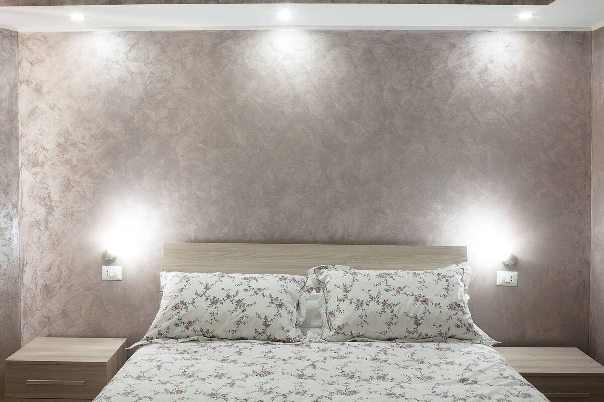A bedroom with a bed, nightstands, and wall-mounted lights.