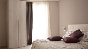 Um quarto com cama, almofadas, mesa de cabeceira e guarda-roupa.