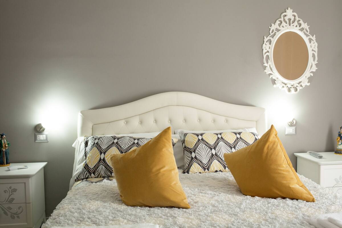 A bedroom with a tufted headboard, patterned bedding, and two bedside tables with lamps.