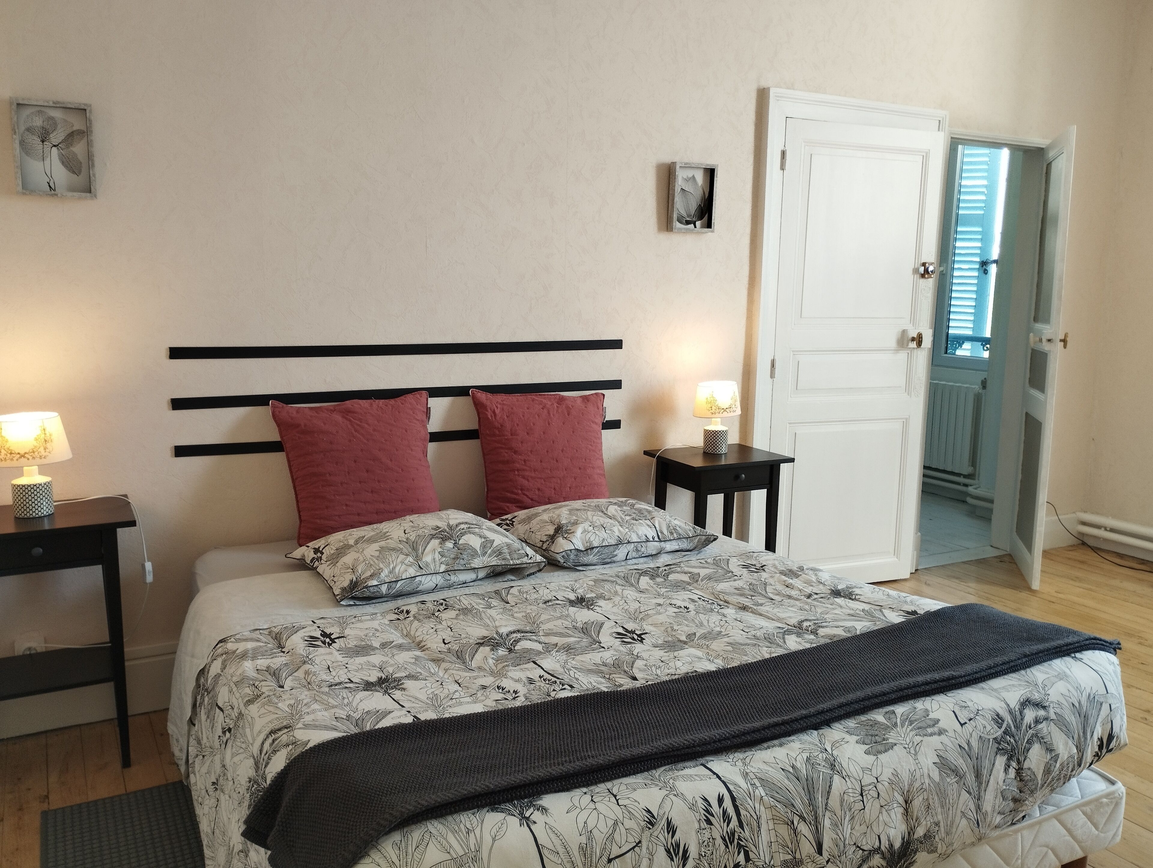 Un dormitorio con una cama, dos mesitas de noche, una mesilla, una puerta y una ventana con persianas.