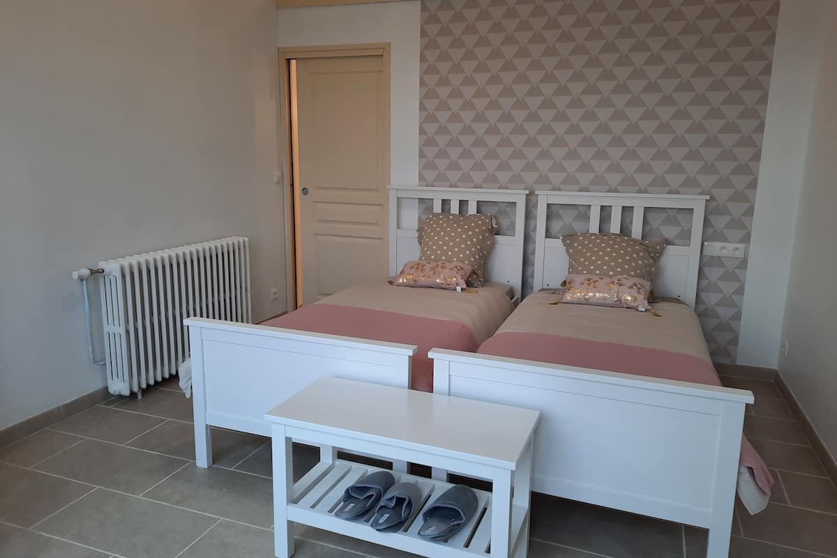 Ein Schlafzimmer mit zwei Betten, einem Heizkörper, einem kleinen Tisch mit Schuhen und einer Tür.
