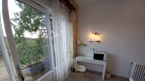A small, clean room with a white desk, a chair, a window with curtains, and a wall-mounted light fixture. - Villa du Cerf Thibault (Le Blanc)