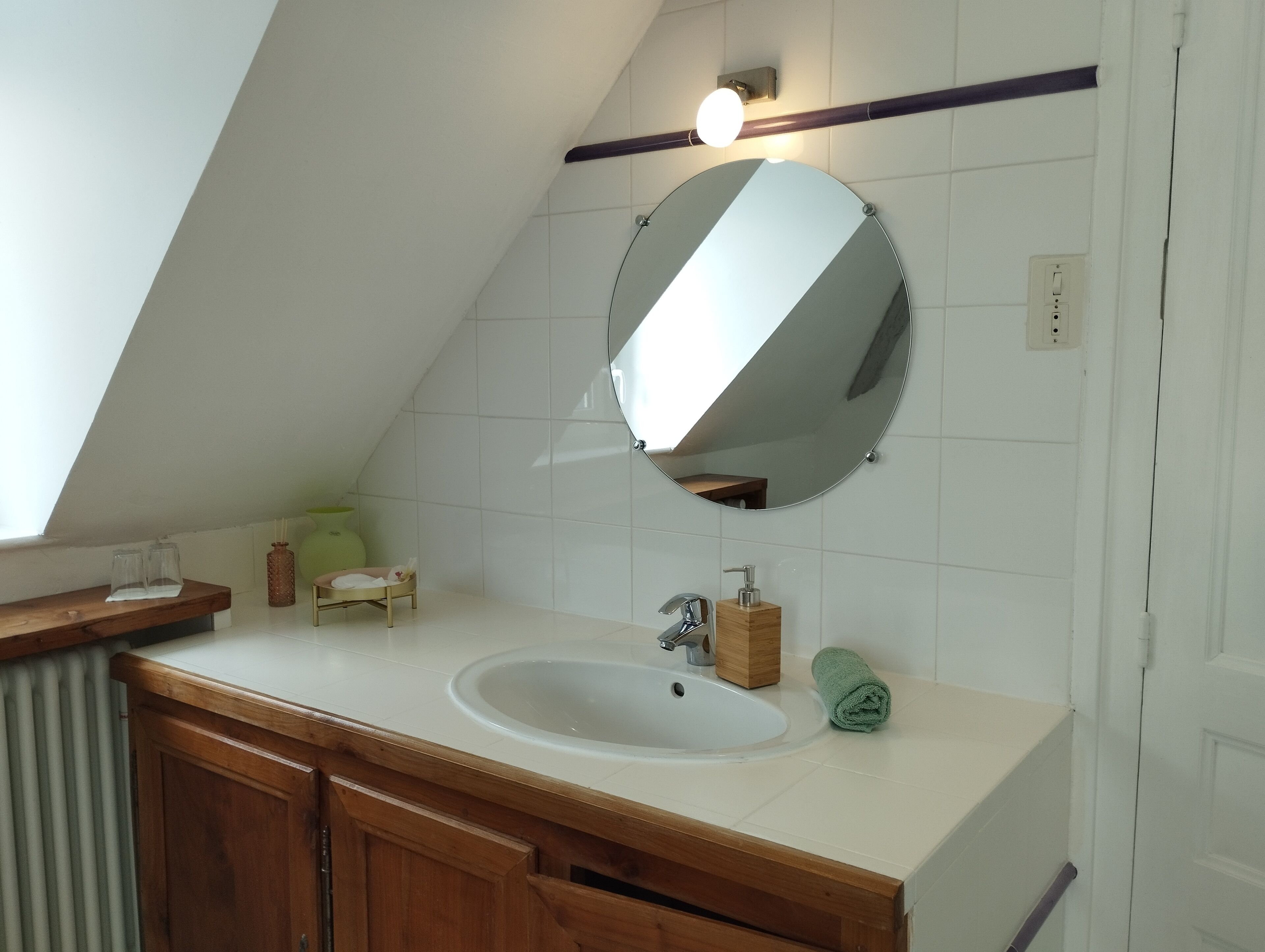 Een badkamer met een witte wastafel, houten opbergmeubel, een ronde spiegel en een handdoek.