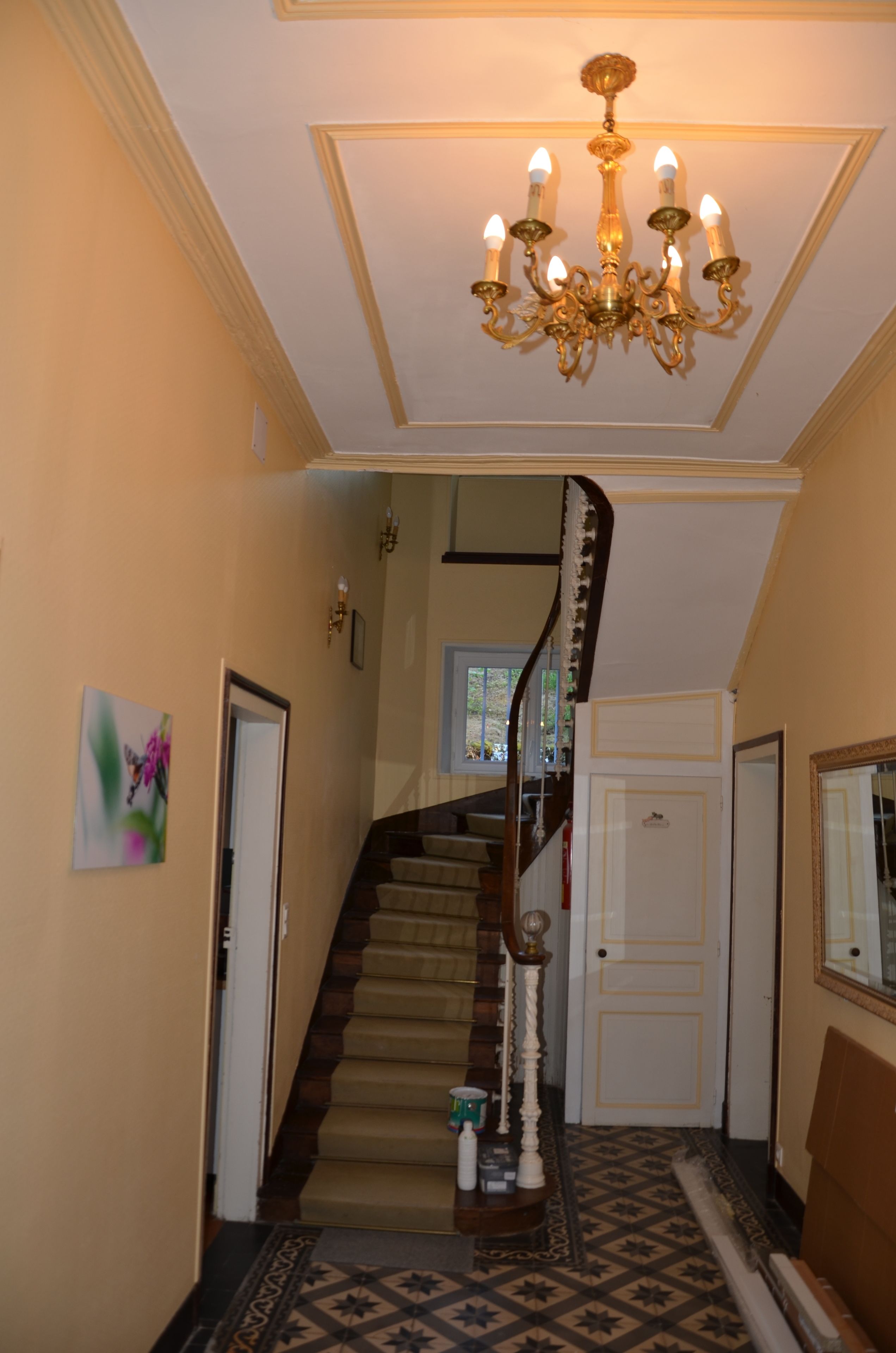 A staircase with a chandelier, a door, and a painting on the wall.