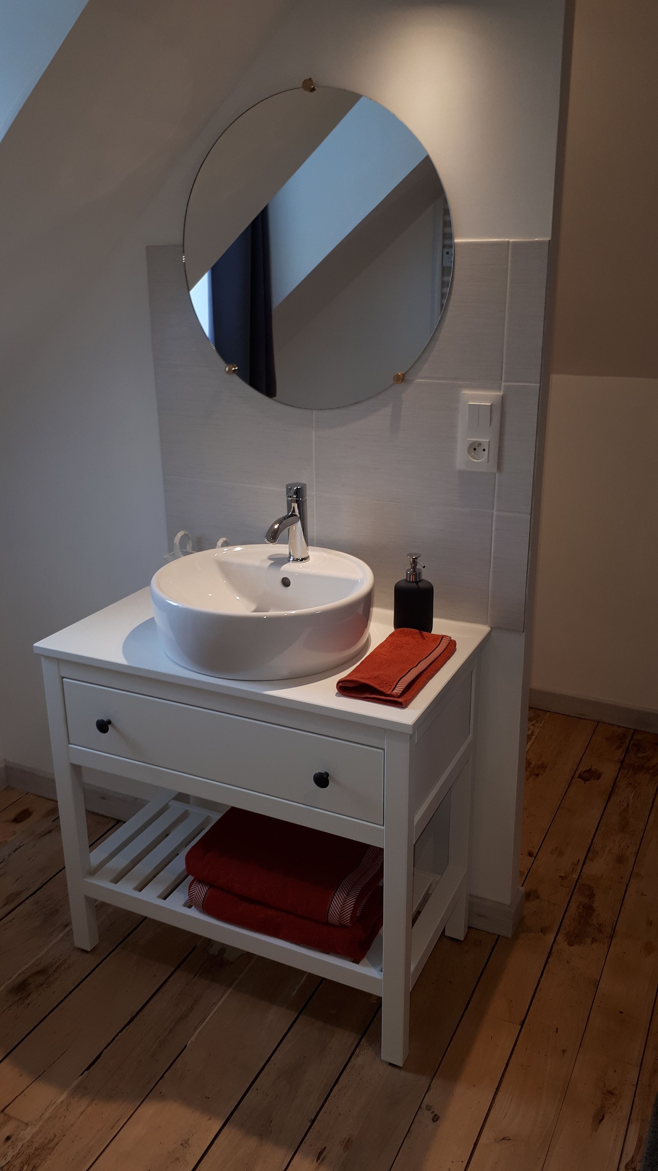 Un bany amb un lavabo blanc, un mirall rodó, un lavabo blanc i una tovallola vermella.