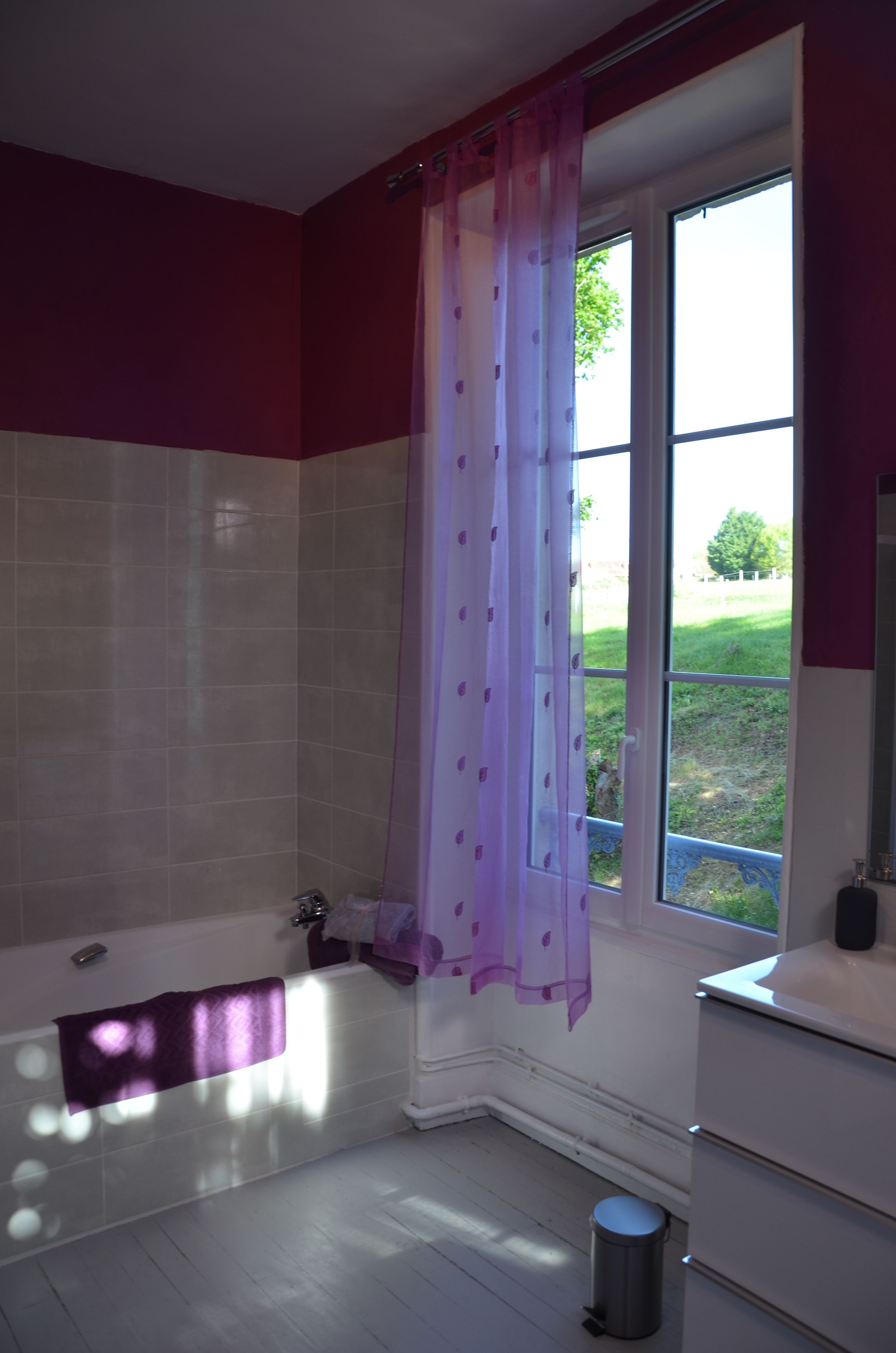 Une salle de bain avec une baignoire, une fenêtre donnant sur l’extérieur et une poubelle.
