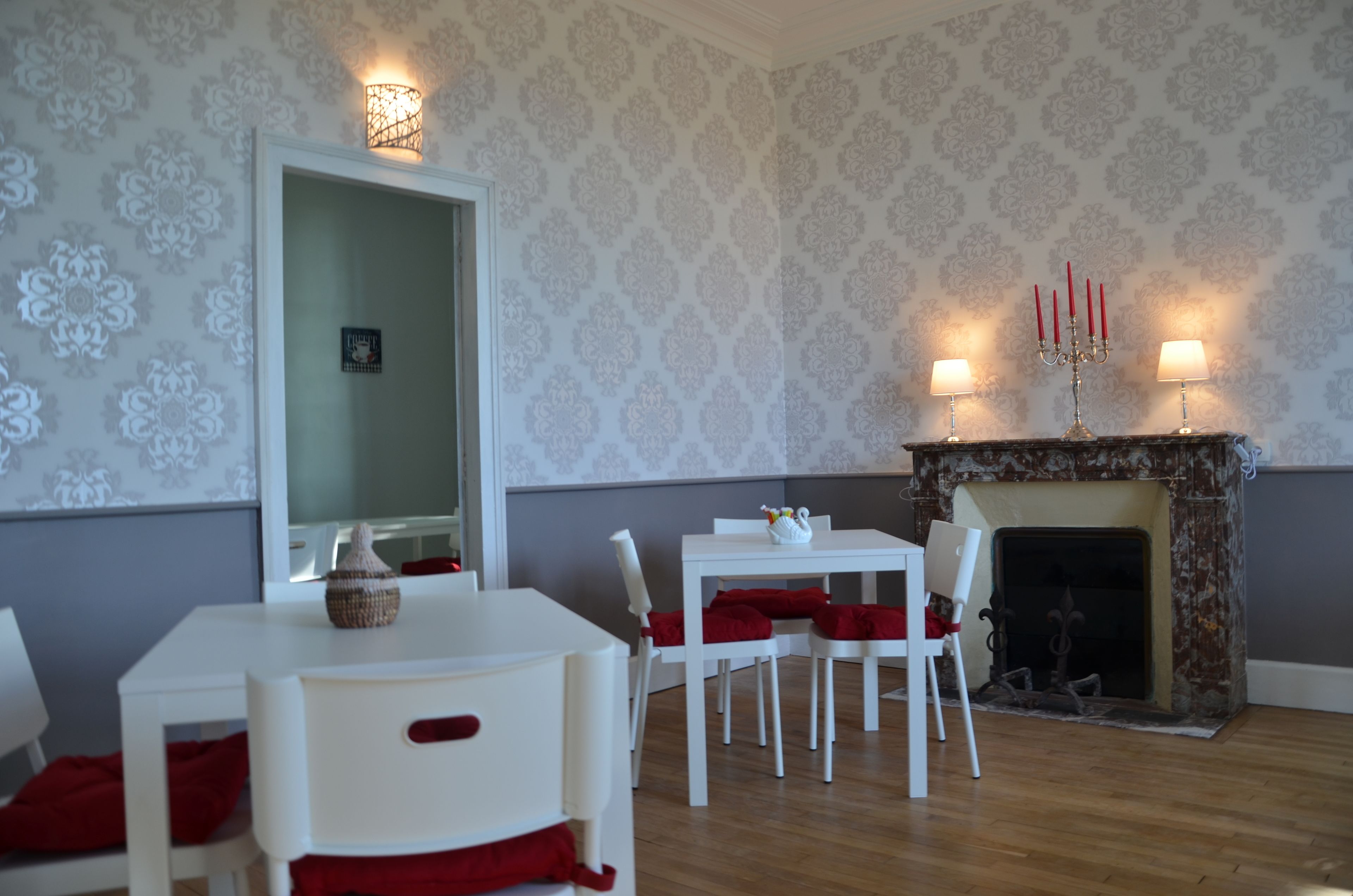 Un comedor con una mesa y sillas blancas, una chimenea con velas rojas y papel tapiz estampado.
