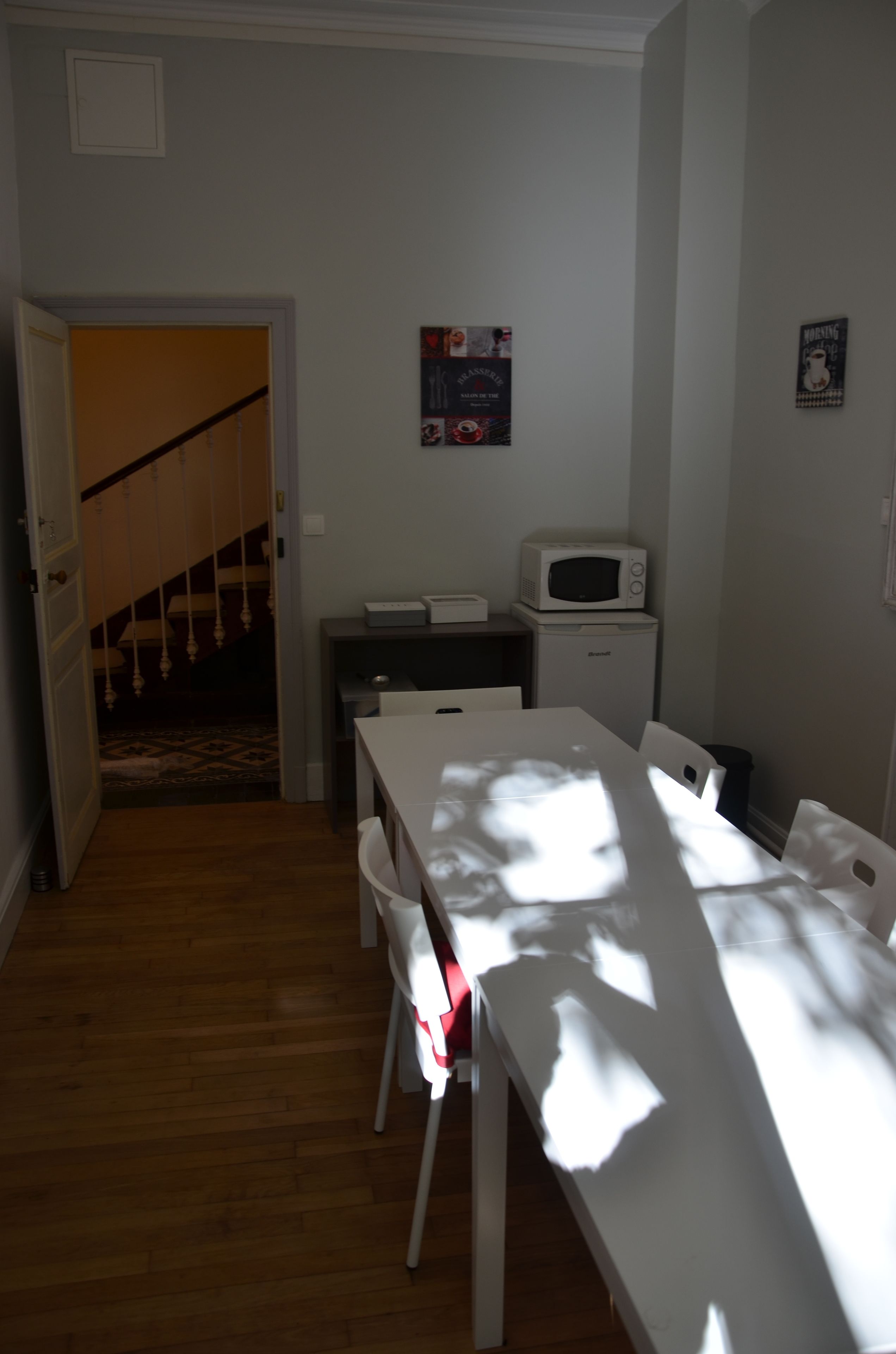 A room with a dining table, chairs, a microwave, and a small refrigerator. A staircase is visible in the background.