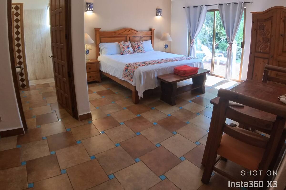 A bedroom with a bed, bedside tables, a ceiling fan, and a view of the outdoors through a window.