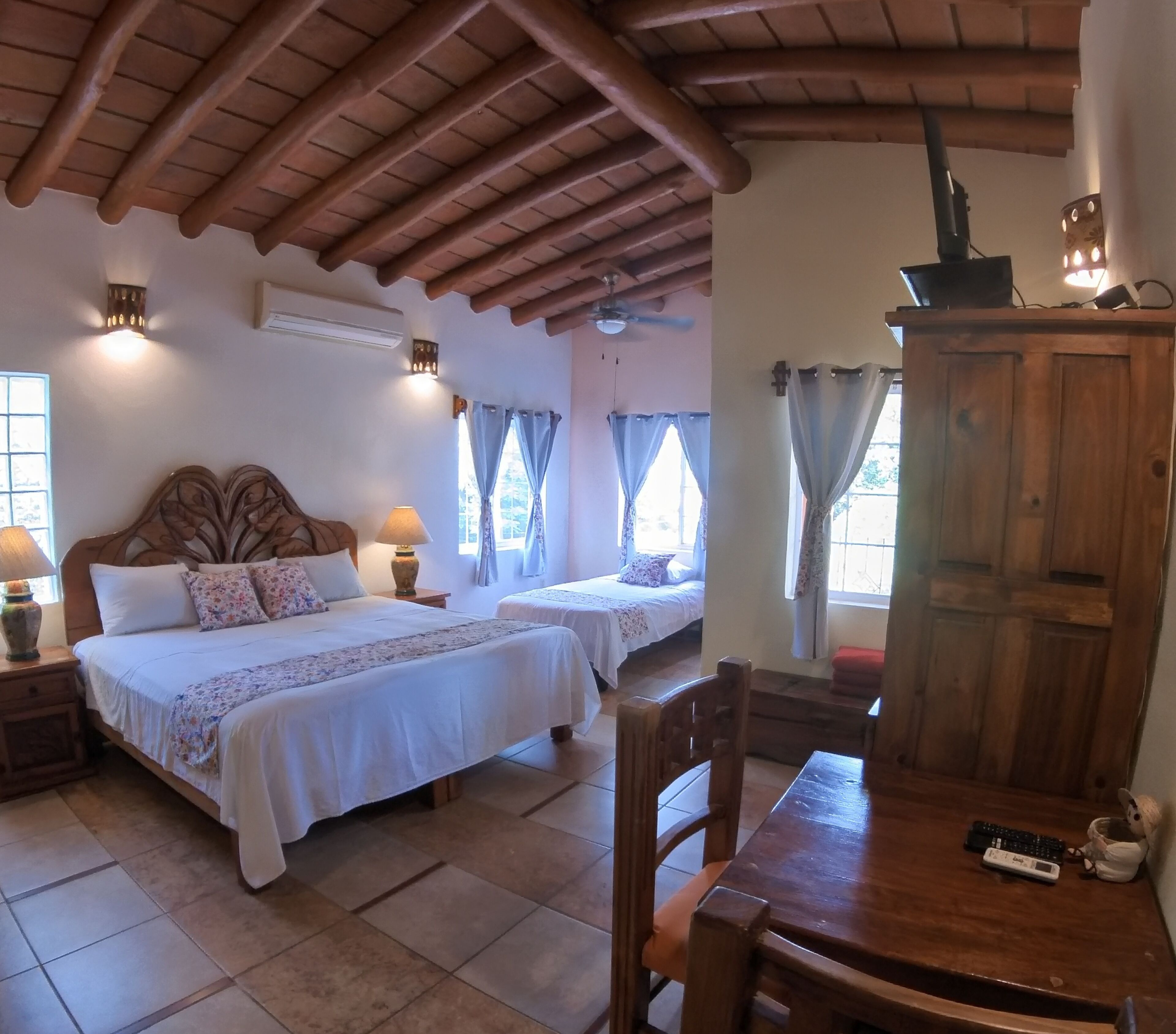 A room with two beds, a wooden ceiling, a table, and a cabinet.