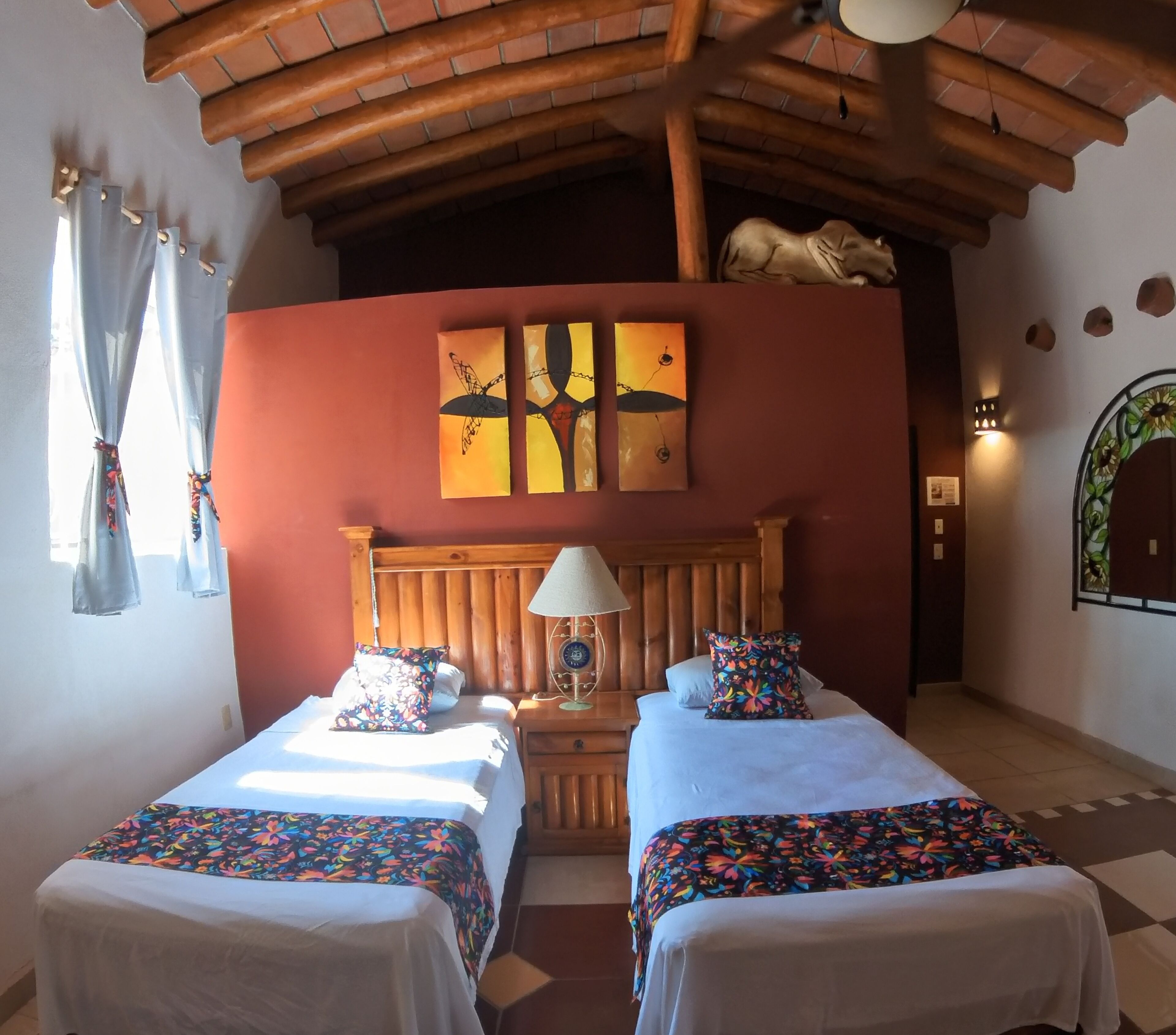 A room with two beds, a wooden headboard, a wall-mounted lamp, and a decorative wall piece.