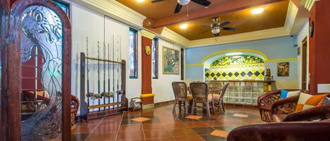 A spacious room with a tiled floor, a ceiling fan, a dining area with chairs, and a bar area with a counter.