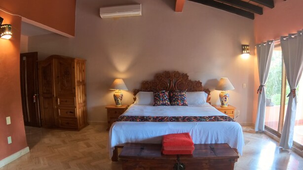 A bedroom with a wooden bed, two bedside tables with lamps, a wooden wardrobe, and a bench. - Casa Virgilio B&B (Nuevo Nayarit)